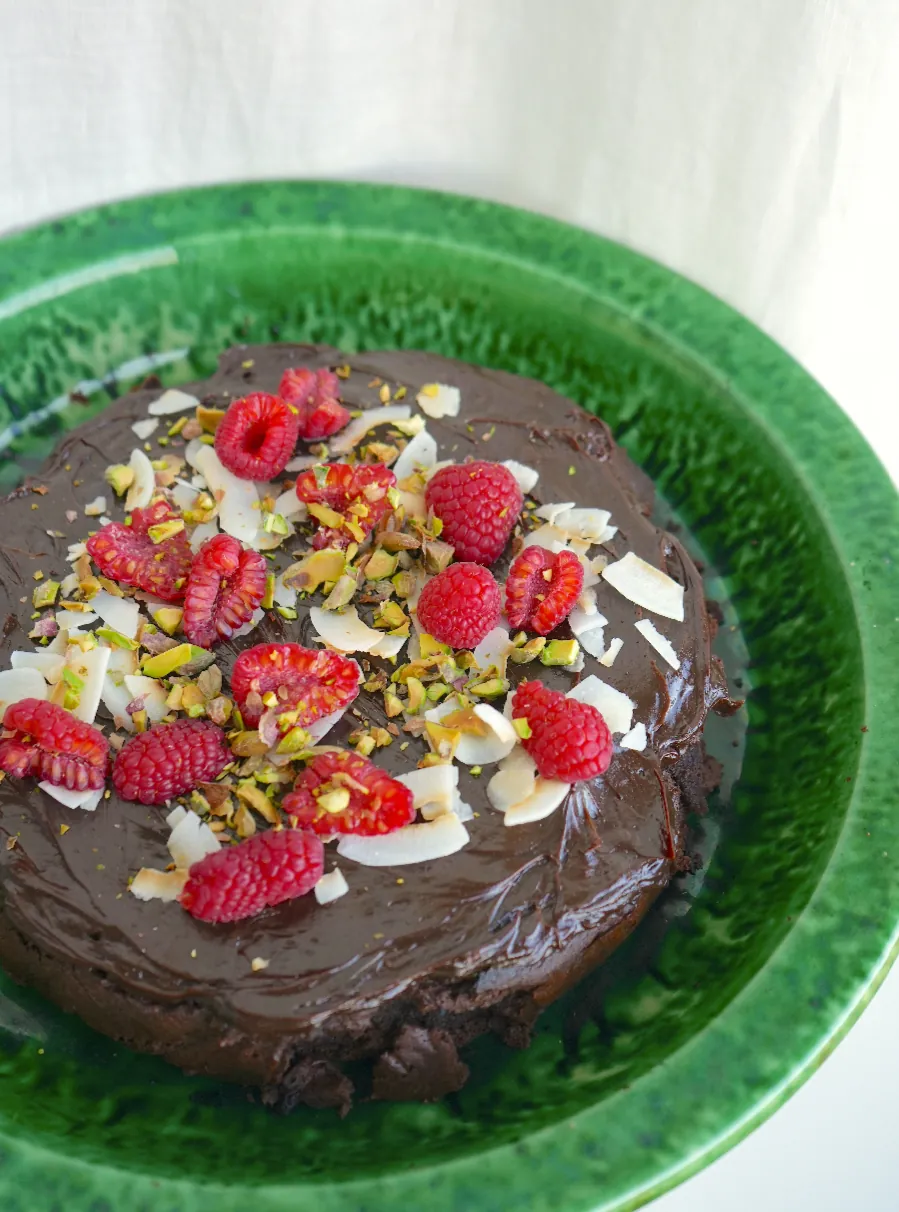 A chocolate cake with raspberries, pistachio and coconut on a green plate