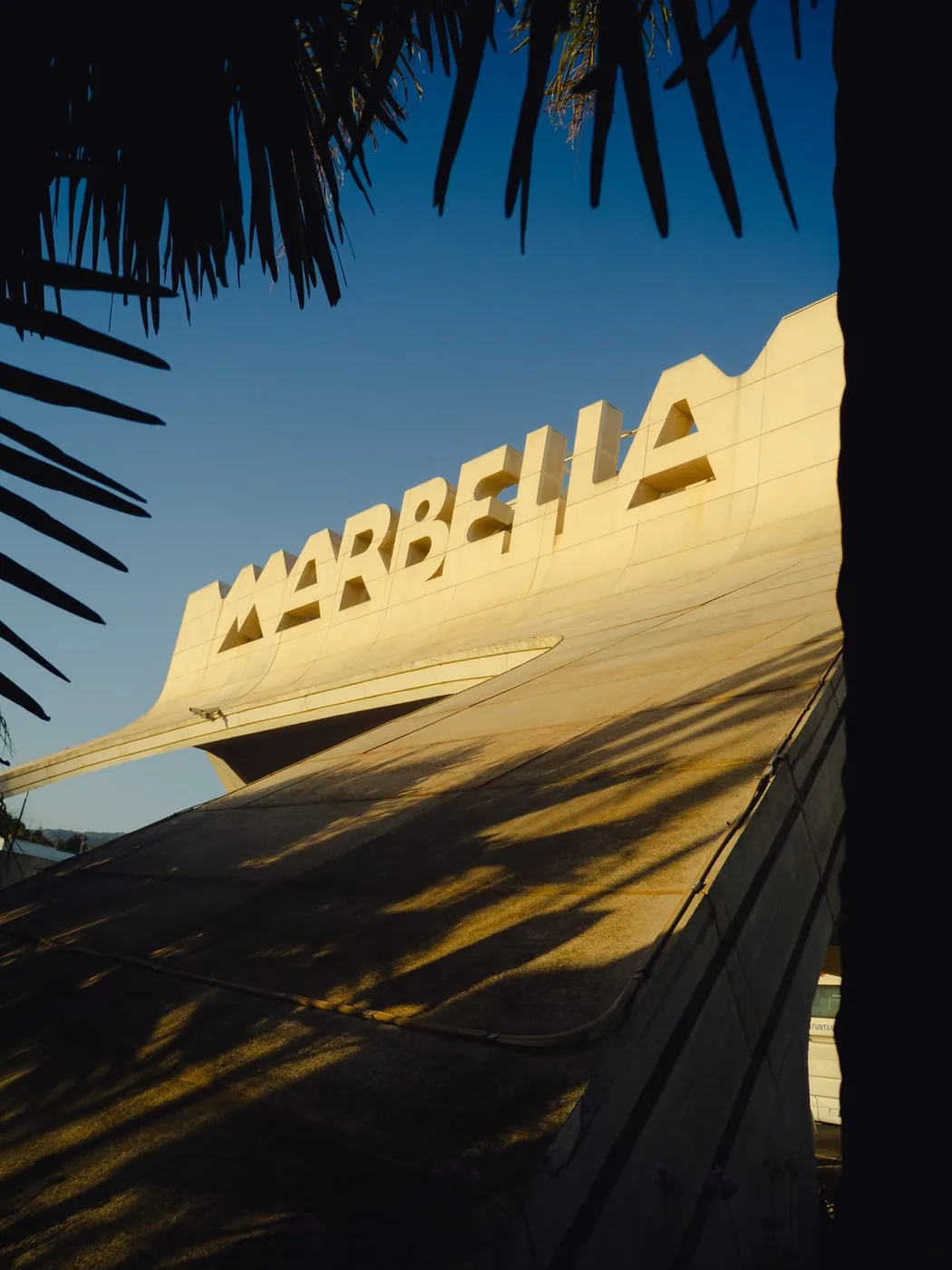 The Marbella sign in the evening sun, framed by palm leaves